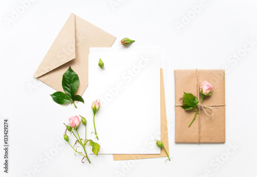 Letter, envelope and gift on white background. Invitation cards, or love letter with pink roses. Holiday concept, top view, flat lay