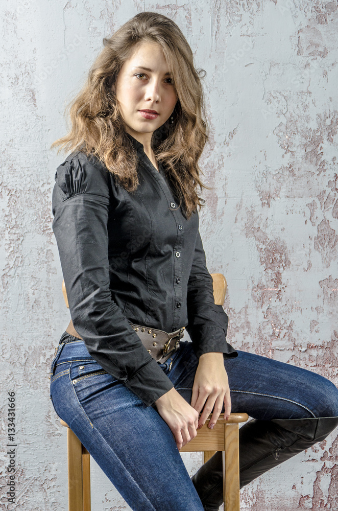Young girl with curly hair in a black shirt, jeans and high boots cowboy western style
