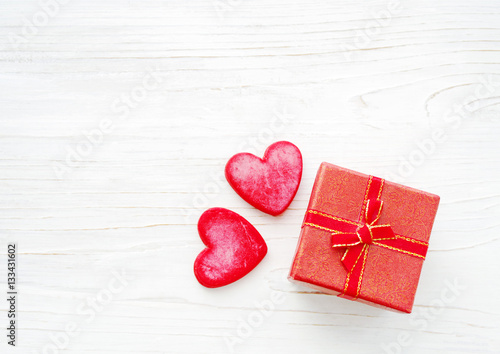 Red hearts and small gift box with a bow on a wooden white background. Greeting card for lovers, friendship or valentine's day.