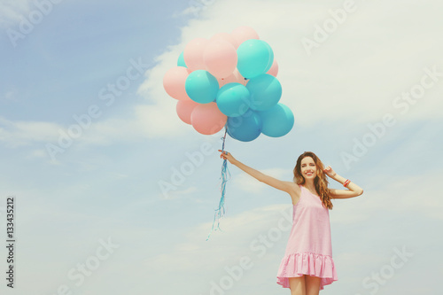 Young woman with colorful balloons on sky background