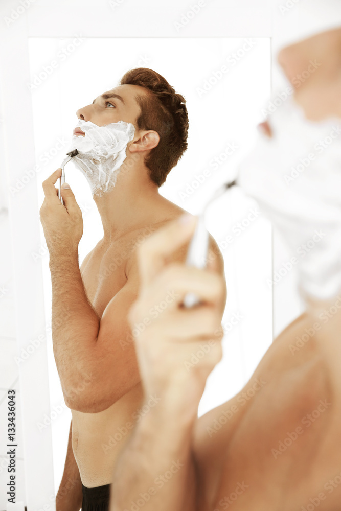 Young handsome man shaving his face in bathroom