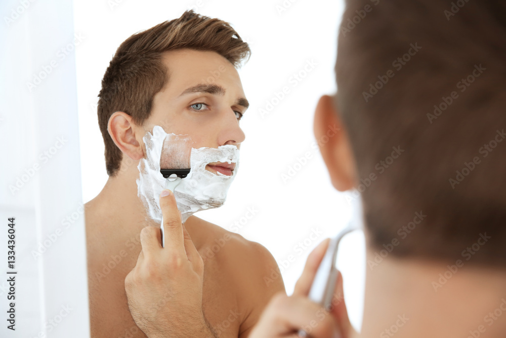 Young handsome man shaving his face in bathroom