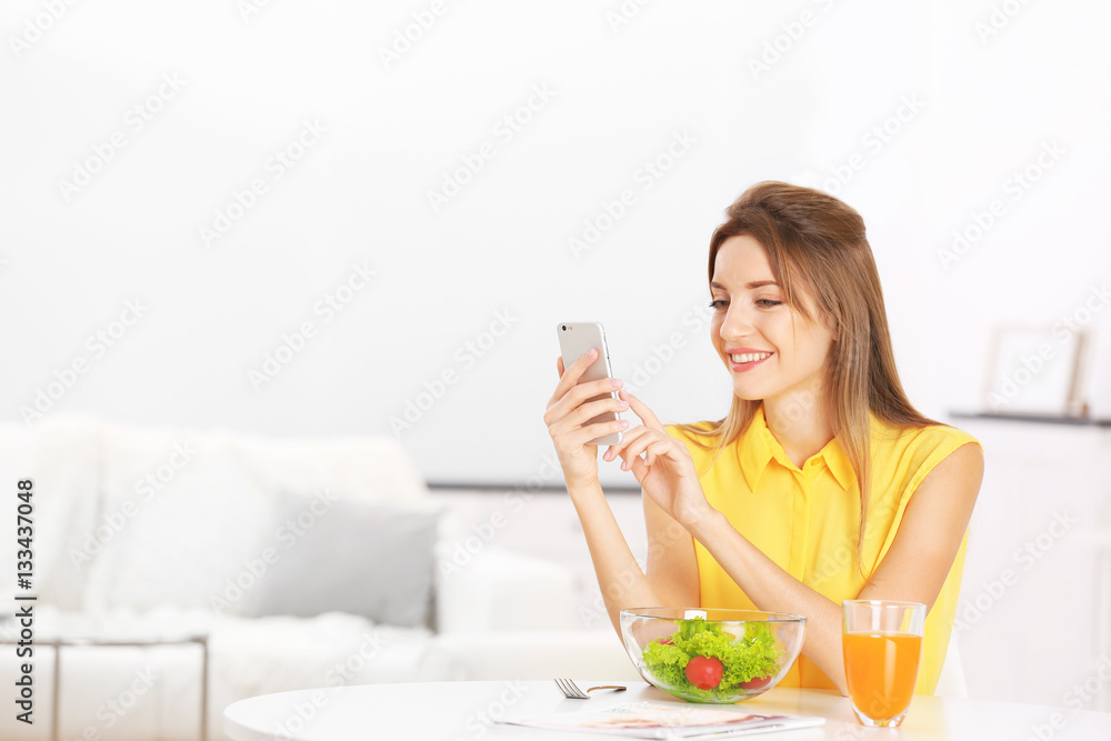Young beautiful woman having breakfast and using smart phone