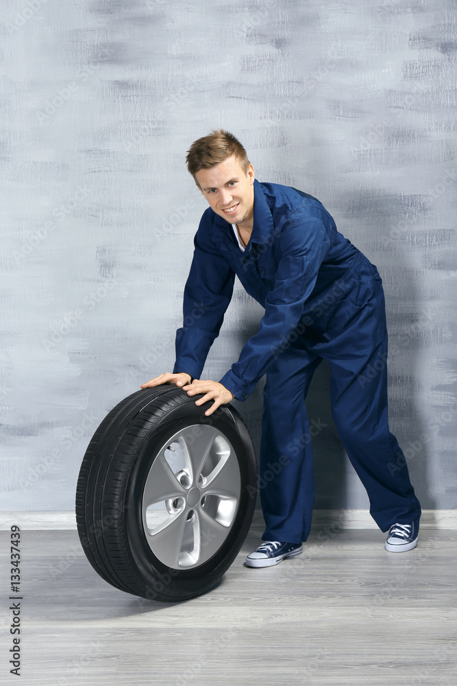 Young mechanic in uniform with wheel, on gray background Young mechanic in uniform with wheel, on gray background