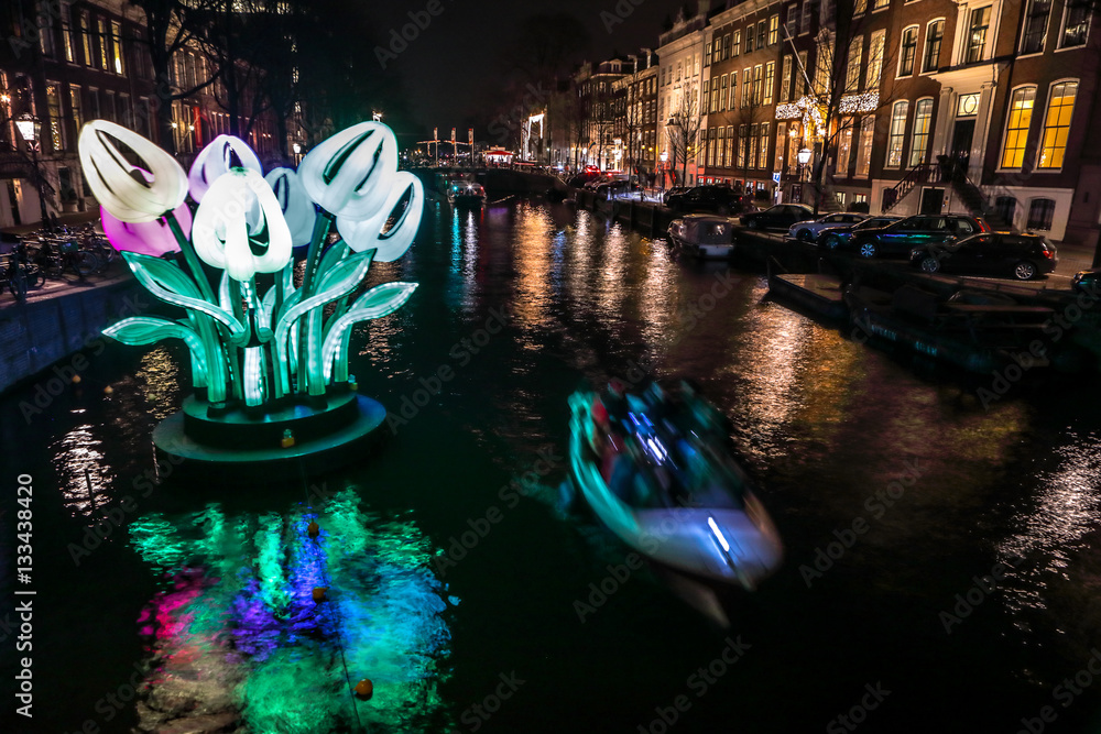 Fototapeta premium AMSTERDAM, NETHERLANDS - JANUARY 11, 2017: Cruise boats rush in night canals. Light installations on night canals of Amsterdam within Light Festival. January 11, 2017 in Amsterdam - Netherland..
