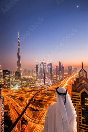 Arabian man watching night cityscape of Dubai with modern futuristic architecture in United Arab Emirates