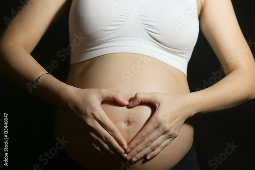 Clouse-up of big pregnant belly with fingers heart symbol