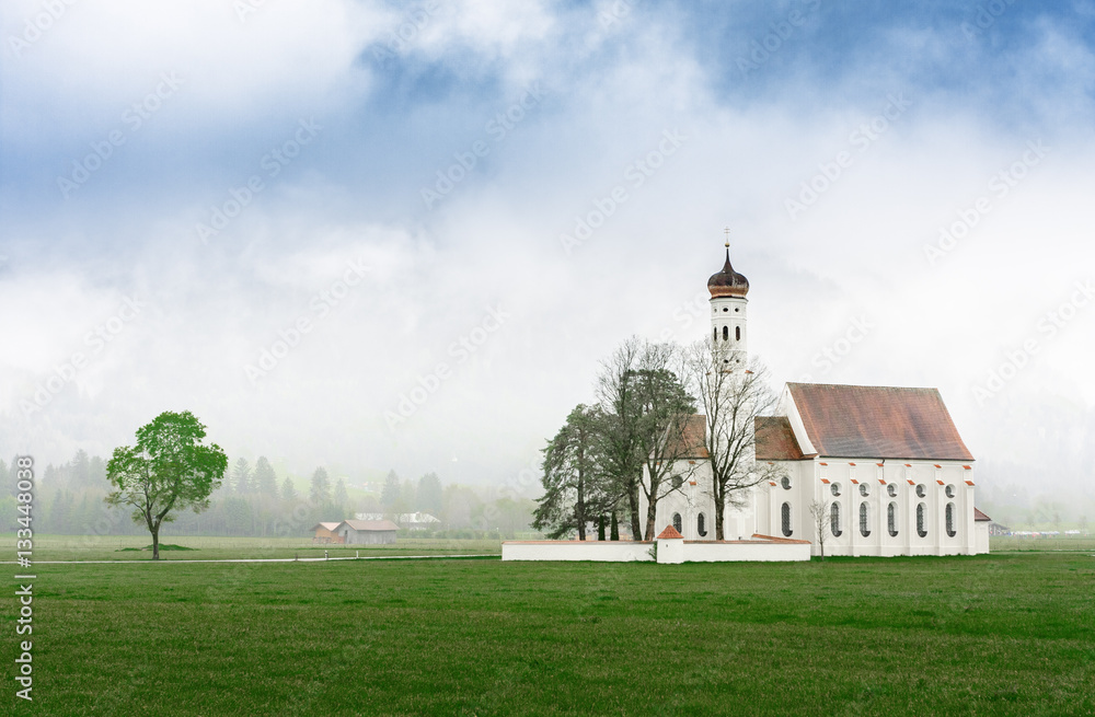 St. Coloman / Schwangau church nearby Neuschwanstein castle in Bavaria region, Germany. Spring misty scene. Green grass meadow at landscape foreground. Place of catholic worship. St. Coloman / Schwangau church nearby Neuschwanstein castle in Bavaria region, Germany. Spring misty scene. Green grass meadow at landscape foreground. Place of catholic worship.