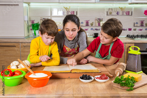 Three kids reading the cook book, making the dinner