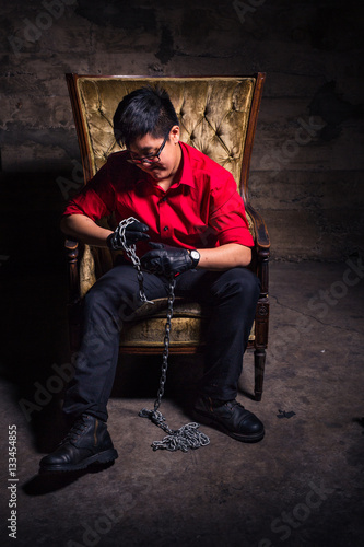Young transgender man in red shirt and leather gloves holding a chain while sitting