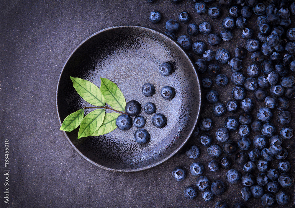 fresh picked blueberries with green of leaf on black stone back fresh picked blueberries with green of leaf on black stone back