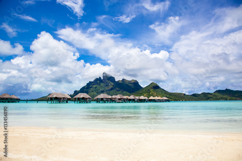 Luxury thatched roof honeymoon bungalows in a vacation resort in the blue lagoon of the Pacific island of Bora Bora  near Tahiti  in French Polynesia.  Villa over water.