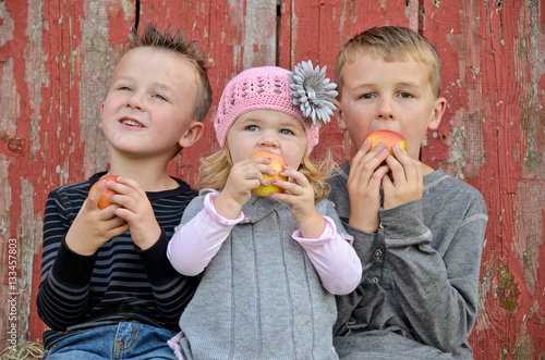 young children eating apples by old red wooden barn