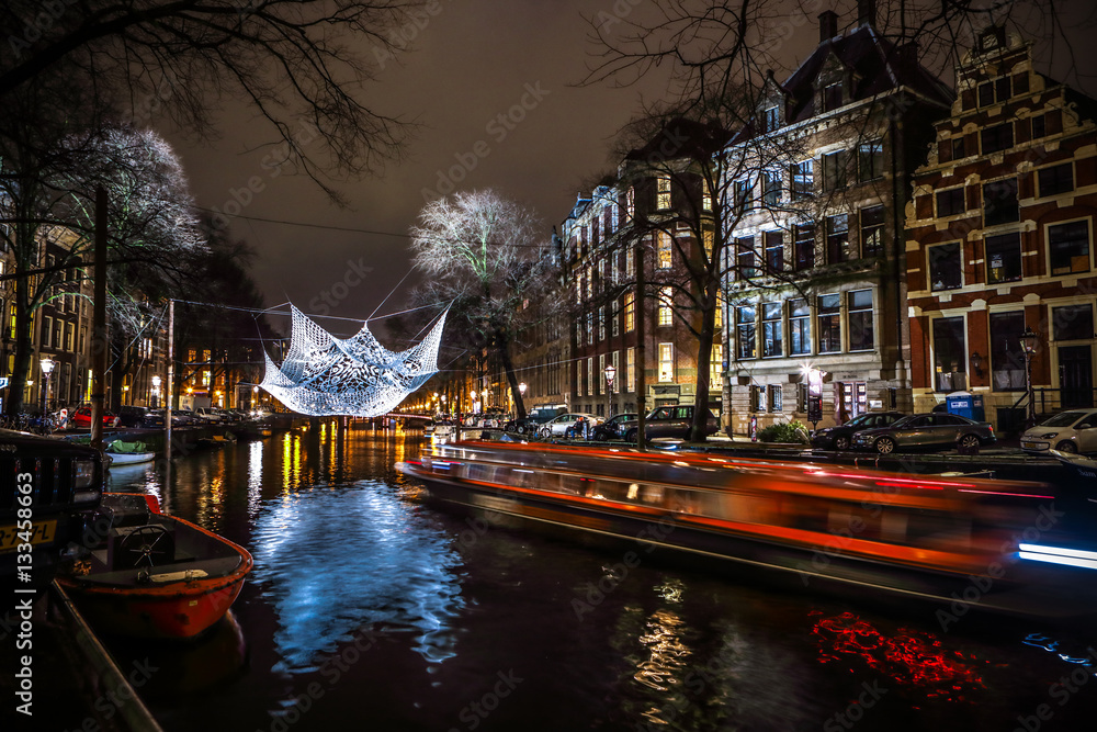 Fototapeta premium AMSTERDAM, NETHERLANDS - JANUARY 12, 2017: Cruise boats rush in night canals. Light installations on night canals of Amsterdam within Light Festival. January 12, 2017 in Amsterdam - Netherland..