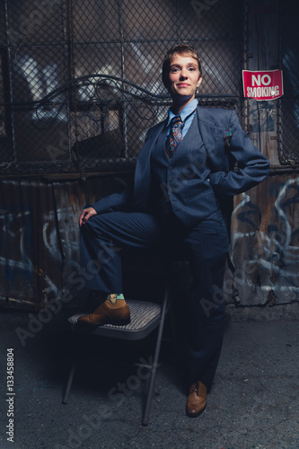 Young androgynous woman dressed in mens clothing in a grungy, urban outdoor location