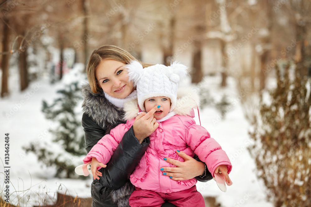 Fototapeta premium Mother and daughter outdoors frost. Mother touching her daughter's nose. Family walk in a winter park. Family happiness.