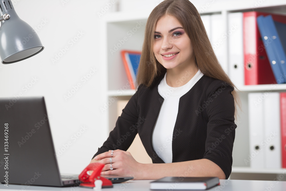 Businesswoman sitting at a desk in the office right shoulder forward. Hands on the table. Looking into the camera. Businesswoman sitting at a desk in the office right shoulder forward. Hands on the table. Looking into the camera.