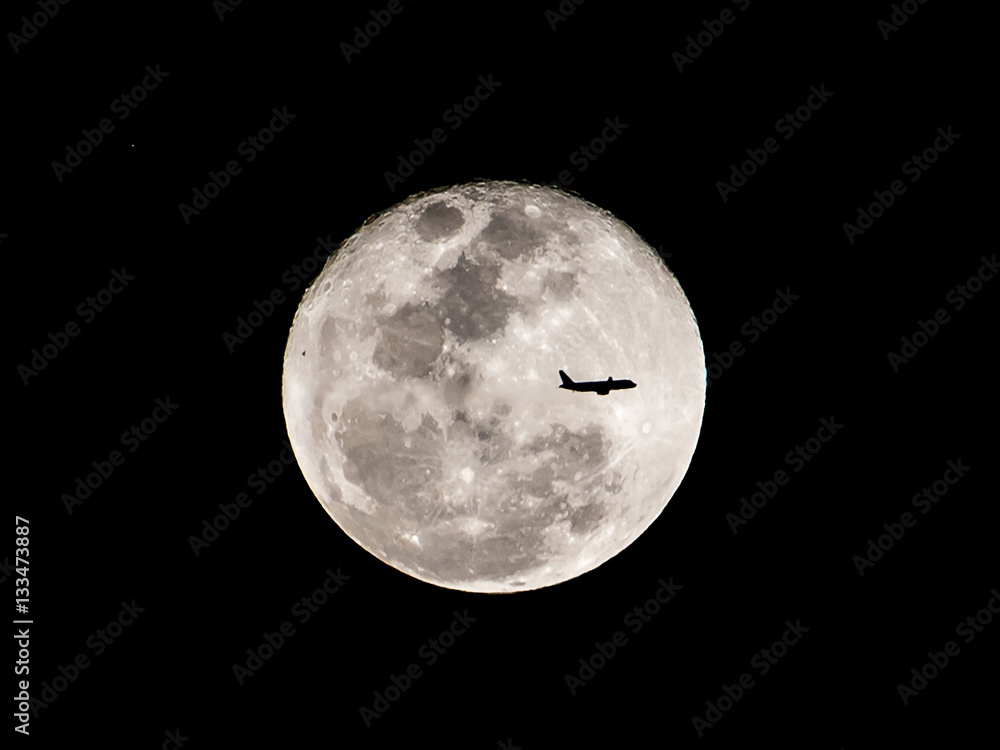 Obraz premium Silhouette of an airplane flying across a full moon.