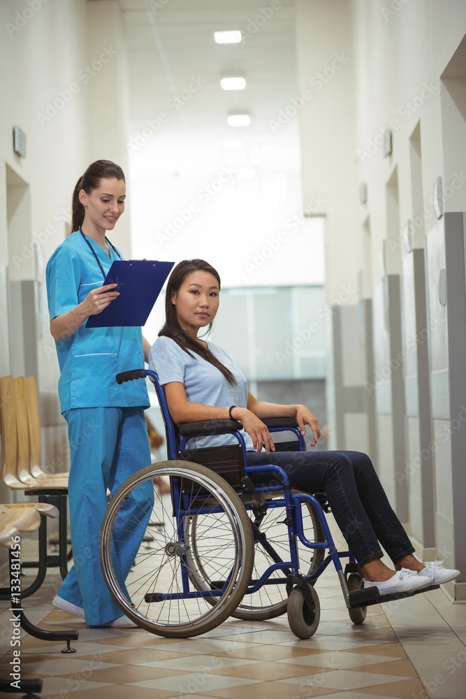 Female nurse assisting patient on wheelchair in corridor Female nurse assisting patient on wheelchair in corridor