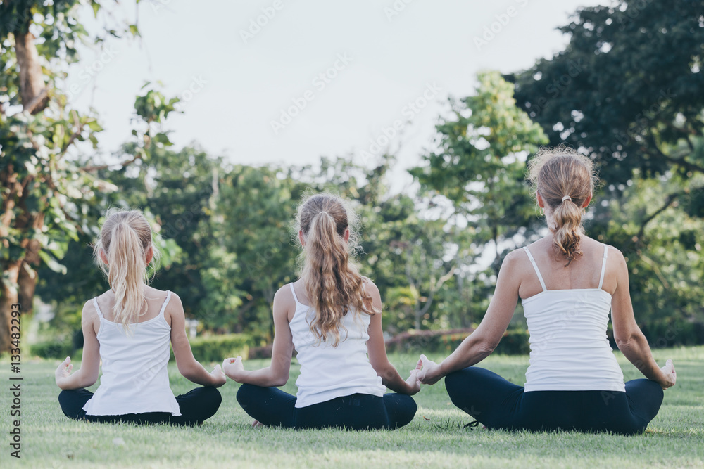 Mother and daughter doing yoga exercises on grass in the park at Mother and daughter doing yoga exercises on grass in the park at