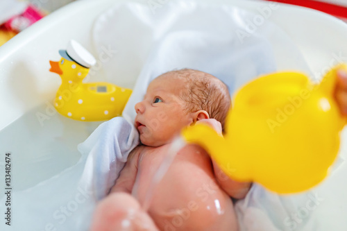Cute adorable newborn baby taking first bath.