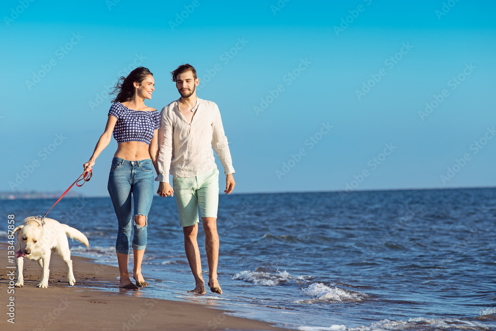 two young people running on the beach kissing and holding tight with dog