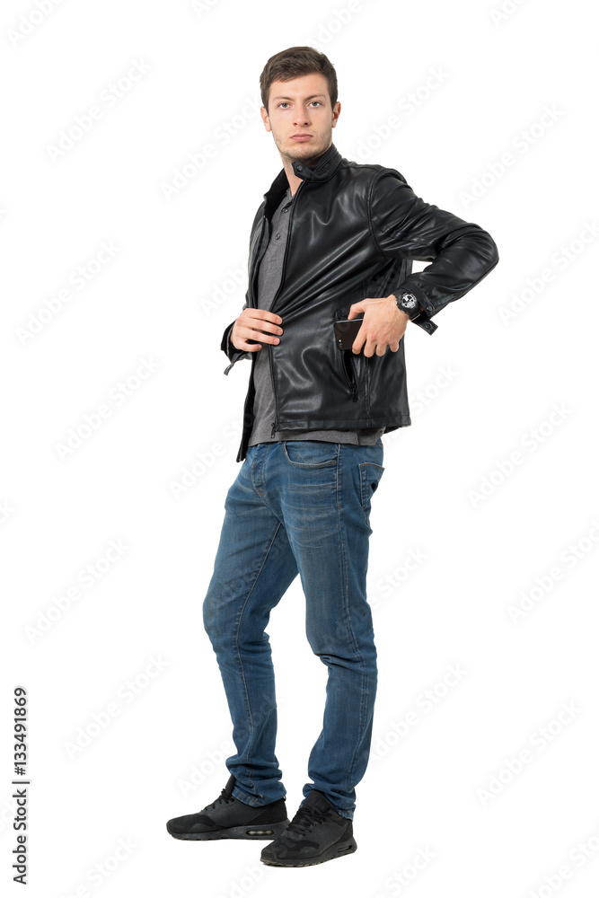 Casual man in jeans and leather jacket put mobile phone inside pocket. Full body length portrait isolated over white background. Casual man in jeans and leather jacket put mobile phone inside pocket. Full body length portrait isolated over white background.