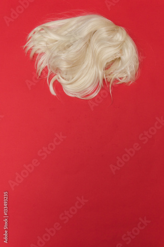 fashion blonde wig on a red background. minimalism. flat lay.