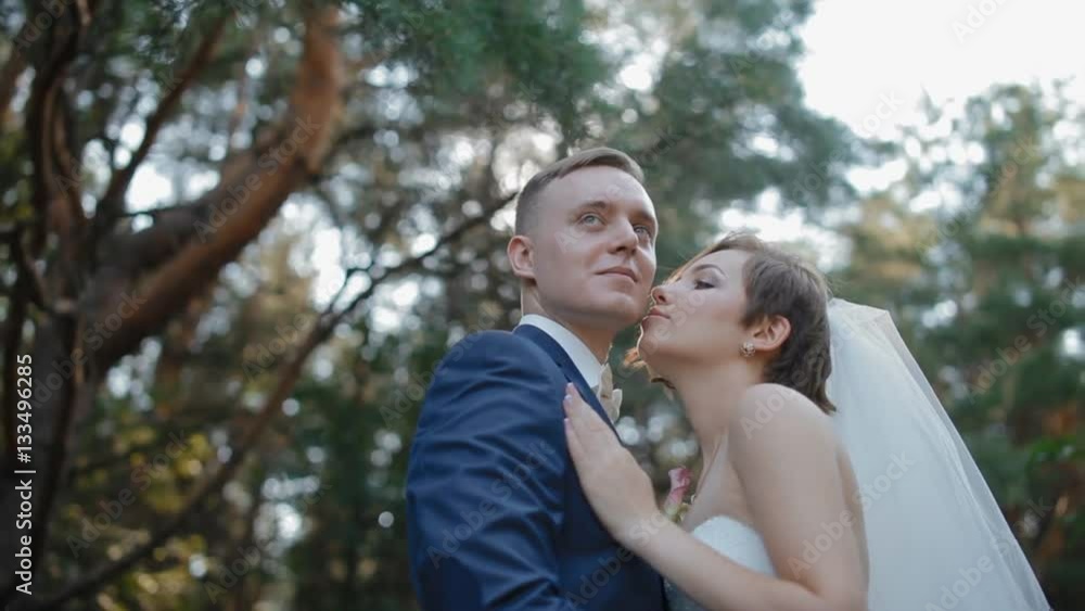 Bride and groom pose in the wood. Young man and woman gently look at each other standing in the forest with sunset light. Beautiful background. Happy moment of loving couple.Middle plan. Bride and groom pose in the wood. Young man and woman gently look at each other standing in the forest with sunset light. Beautiful background. Happy moment of loving couple.Middle plan.