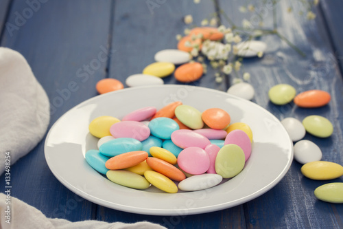 color candies on white plate on wooden background