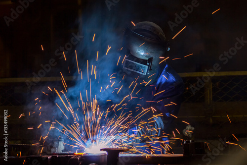 Worker is welding automotive part in car factory