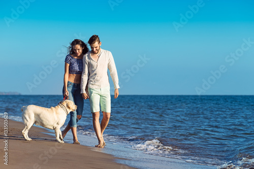 two young people running on the beach kissing and holding tight with dog