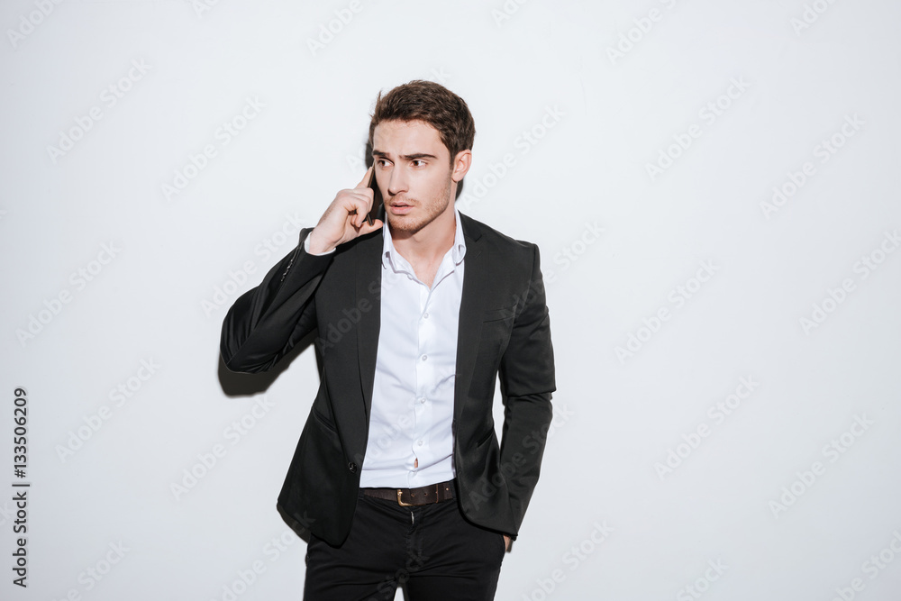 Handsome young businessman posing at studio talking by phone Handsome young businessman posing at studio talking by phone