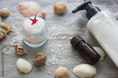 Shell, aromatherapy oil, bottle of body cream and a jar of sea salt on a grey cloth background. Spa concept.