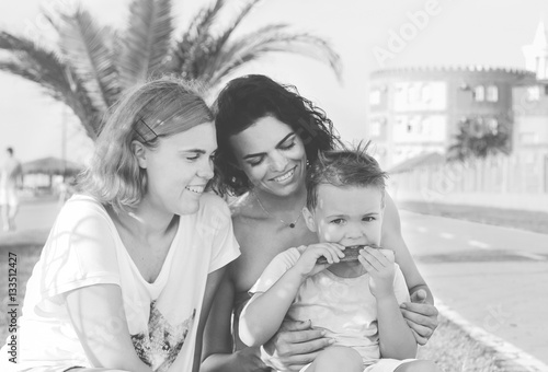 Children with mom sitting and laughing. Boy chewing a stick. Mother holds on hands her son, near smilling daughter. Happy family in summer vacation. Sincere emotions in black and white portrait