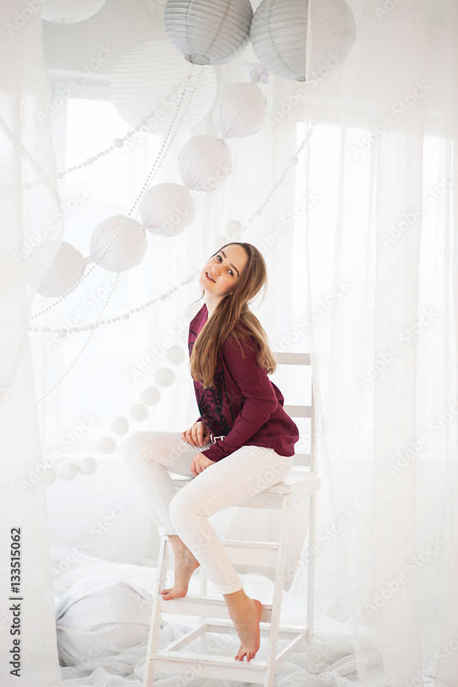 A girl in a cherry sweater sits posing in white decorations A girl in a cherry sweater sits posing in white decorations