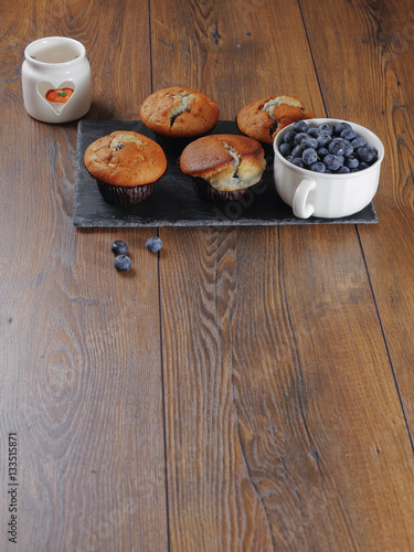 Blueberry muffins and blueberries in a cup on a wooden table.