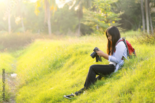 Young woman holding a digital camera  checking a picture result  carrying a backpacker  sitting on a grass or lawn - Traveler concept