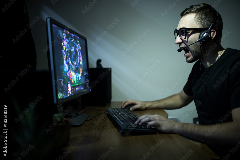 young gamer in headphones and glasses using computer for playing game at home in the night young gamer in headphones and glasses using computer for playing game at home in the night