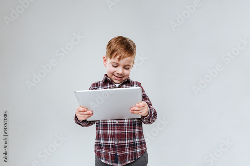 Little child over grey background holding tablet computer.
