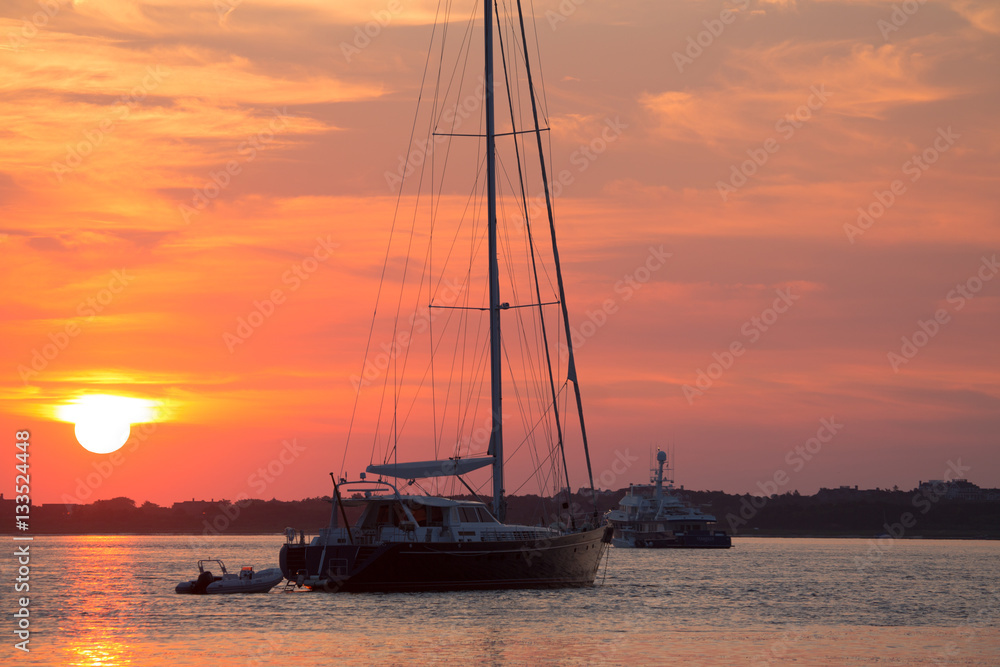 Sunrise along Nantucket harbor with moored large sail boat