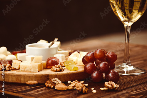 Cheese Board served with grapes, nuts and a glass of white wine on a wooden background