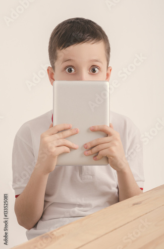 Boy and tablet. The boy holds the tablet covering his face.