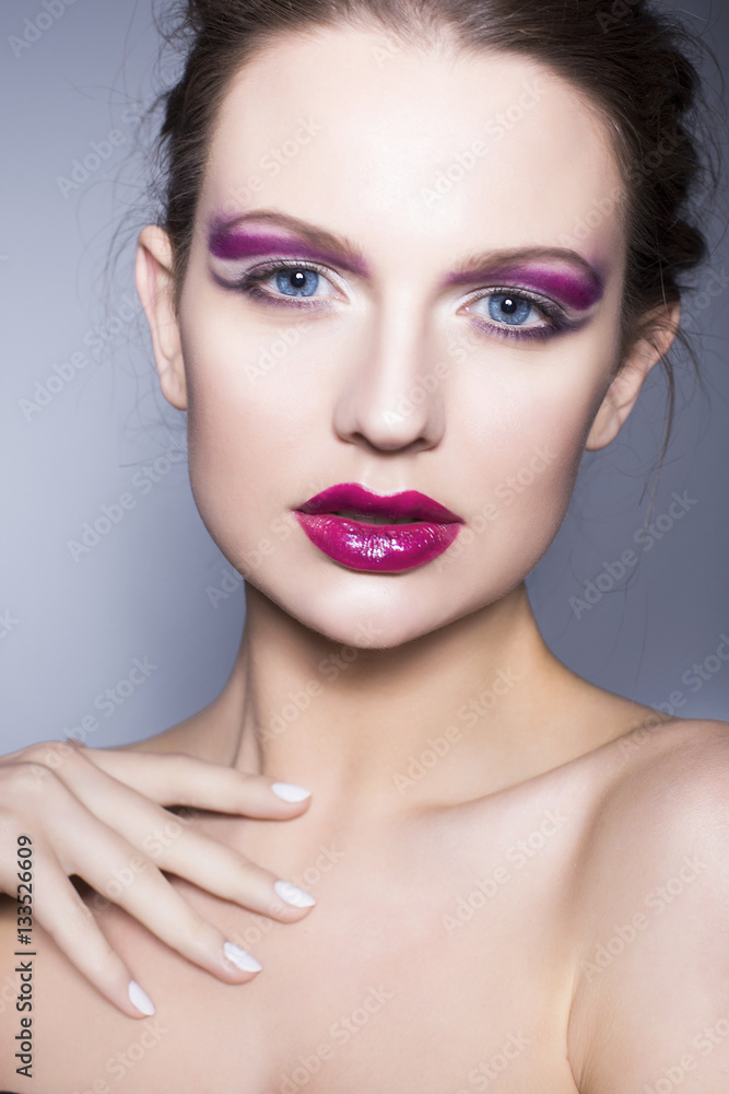 Beautiful brunette woman with creative make up violet eye shadows full red lips, blue eyes and curly hair with her hand on her face