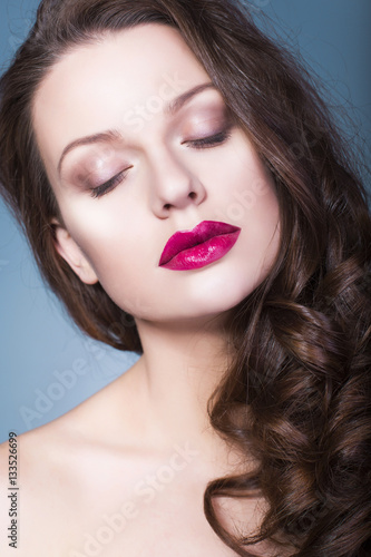 Beautiful brunette woman with creative make up violet eye shadows full red lips, blue eyes and curly hair with her hand on her face