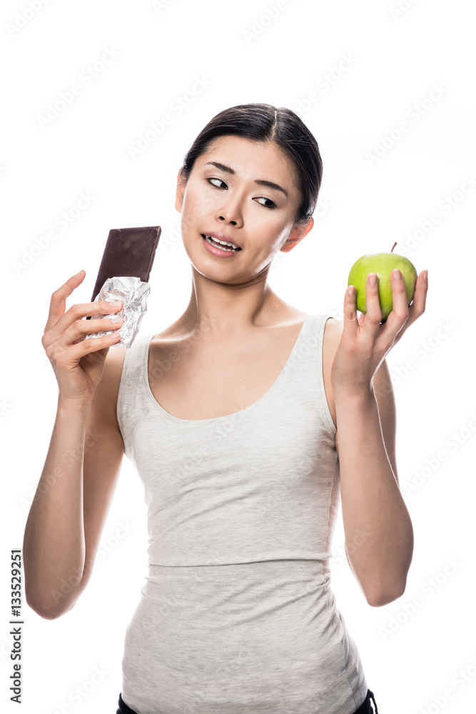 Woman eating a fresh apple while looking at chocolate Woman eating a fresh apple while looking at chocolate