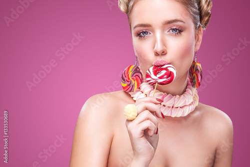Tableau sur toile Attractive woman with lollipop in hand on pink background