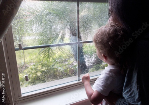 Little boy sits with mother at a window on a rainy day © Yves