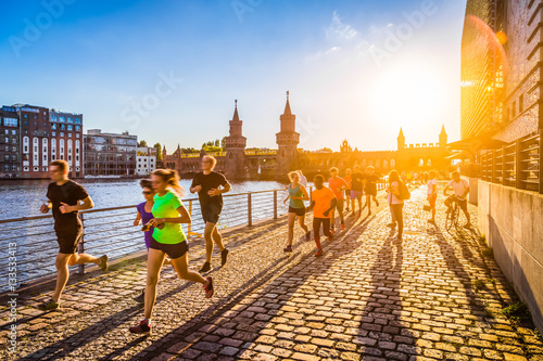 Fototapeta Naklejka Na Ścianę i Meble -  Group of female and male runners jogging in urban area at sunset