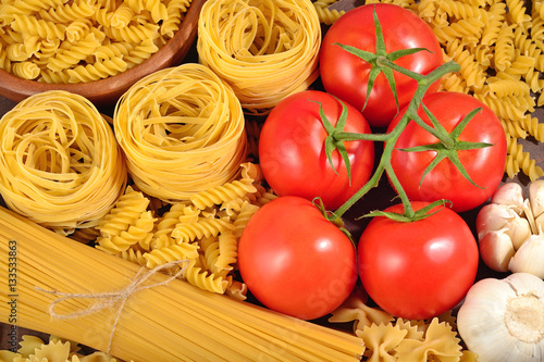 Uncooked Italian pasta, ripe tomatoes branch, and garlic